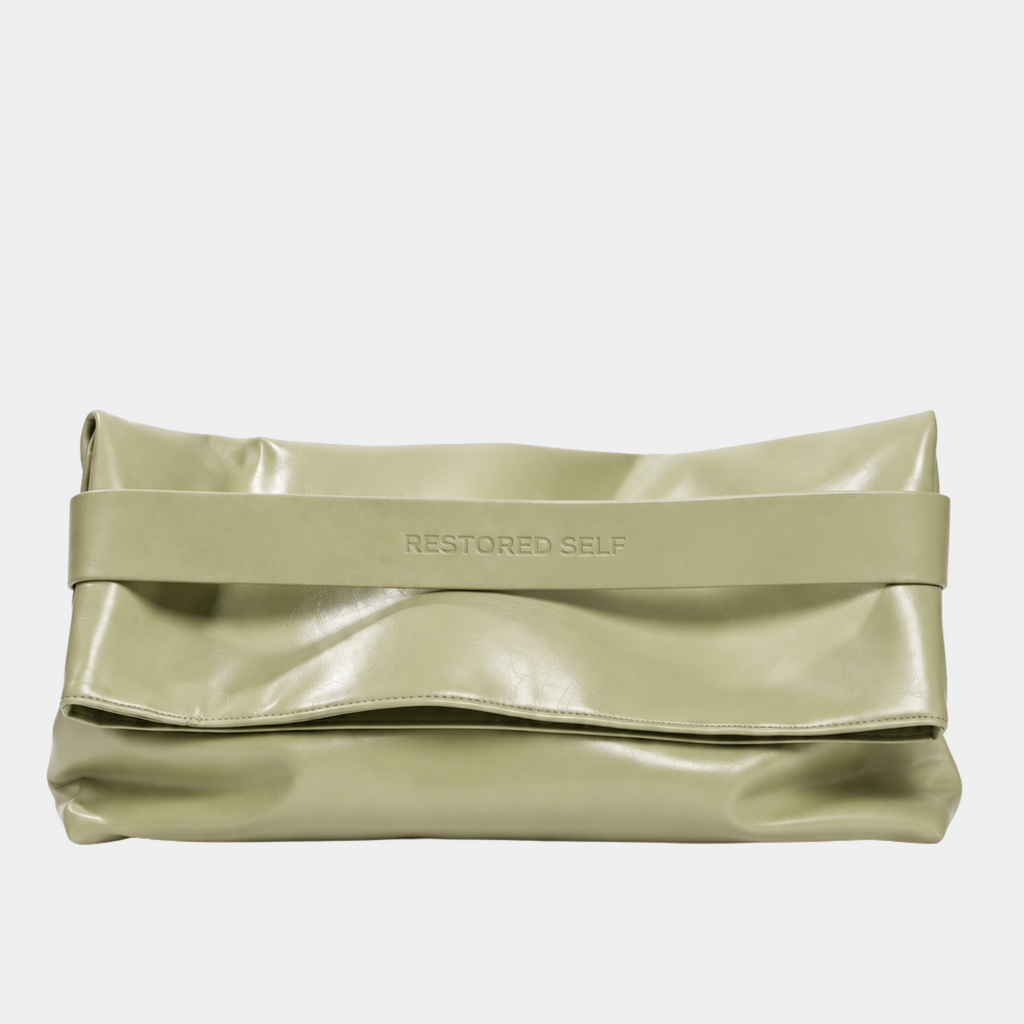 The OG bag in Butter Pistachio, folded as an oversized sage green vegan leather clutch with Restored Self logo band