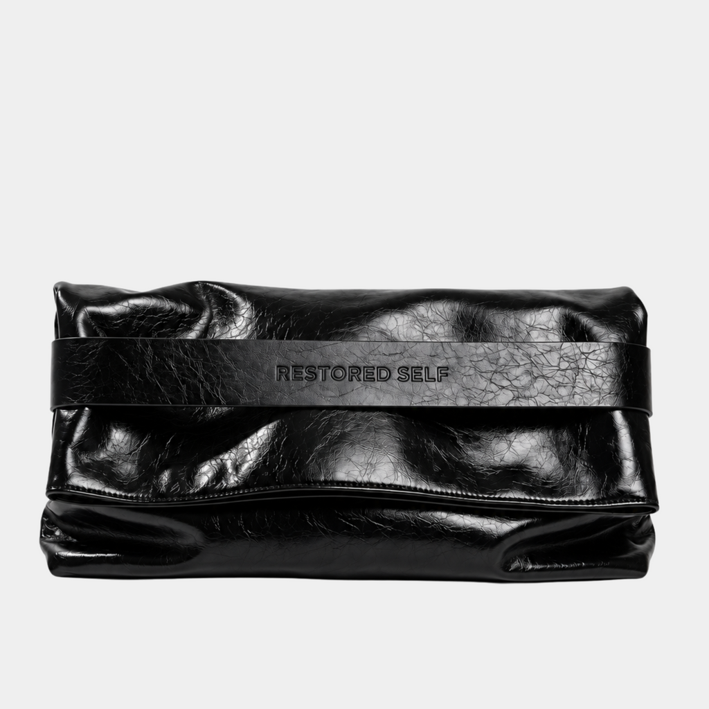 The OG bag in Ink, folded as an oversized black vegan leather clutch with Restored Self logo band